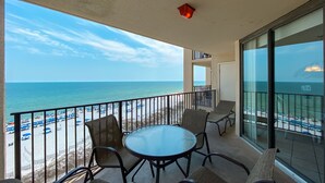 Ein Balkon mit Glasgeländer, der auf einen Strand mit Sonnenschirmen und Liegestühlen blickt.