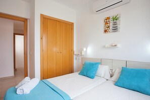 A hotel room with a wooden wardrobe, a bed with blue and white bedding, and a wall-mounted air conditioner. - Marina dór IV, house 5, wifi 5 bedrooms, community pool, beach 300m away (Santanyí)