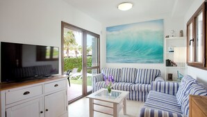 A living room with a TV, striped sofa, glass coffee table, and a painting of a wave. - Marina dór IV, house 5, wifi 5 bedrooms, community pool, beach 300m away (Santanyí)