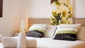A neatly made bed with white linens, two pillows with green and black stripes, and a wall-mounted floral painting. - Marina dór IV, house 5, wifi 5 bedrooms, community pool, beach 300m away (Santanyí)