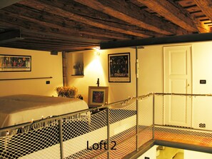 A loft bedroom with a bed, a small table, and a chair. There is a white door and a window with a view of the outside. - Loft in San Lorenzo, two minutes from the aquarium; with parking possibility (Genova, Liguria)