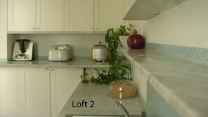 Et køkken med hvide skabe, en brødrister, en blender, en plante og en brødlimpa på bordet.