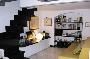 A loft with a staircase, a desk with a computer, a bookshelf, and a yellow couch. - Loft in San Lorenzo, two minutes from the aquarium; with parking possibility (Genova, Liguria)