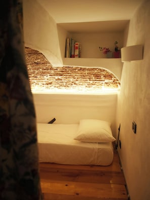 A small, cozy loft bedroom with a single bed, a shelf with books, and a brick wall. - Loft in San Lorenzo, two minutes from the aquarium; with parking possibility (Genova, Liguria)