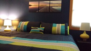 Un lit avec une couvre-lit à rayures, plusieurs oreillers et un tableau accroché au-dessus.