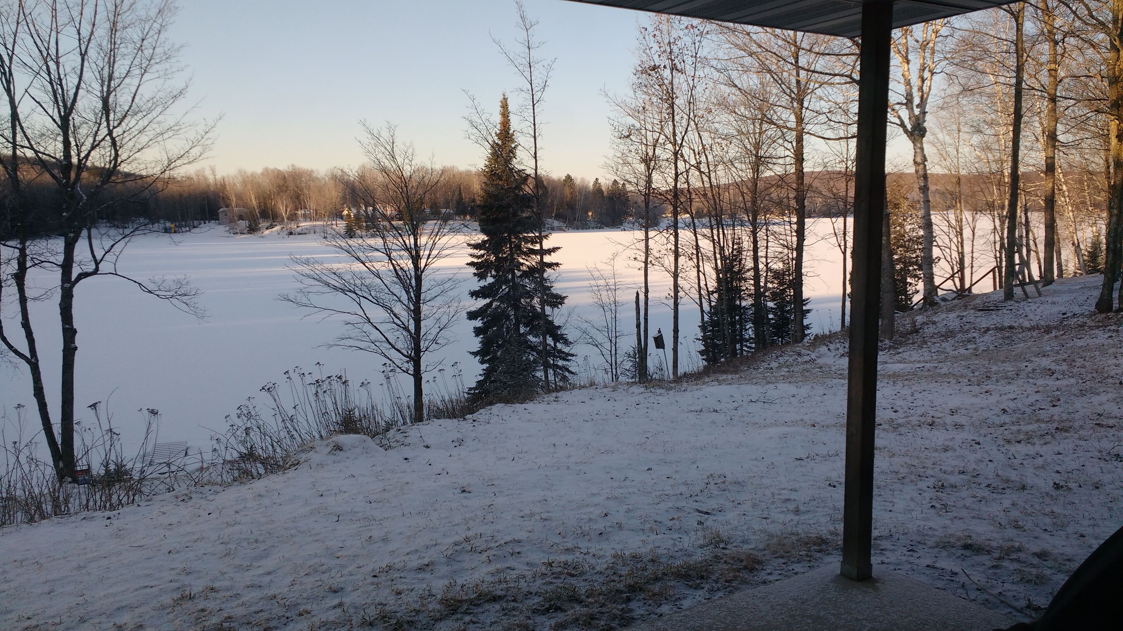 A snow-covered landscape with a frozen lake, trees, and a wooden structure.