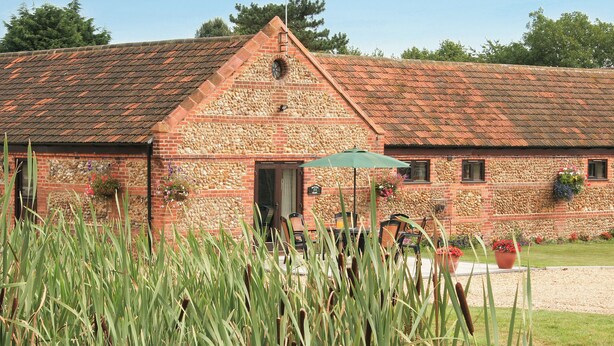 A rustic building with a stone facade, a pitched roof, and a small porch area with outdoor seating. - Baileys Barn - UKC3738 (Foxley, near Fakenham)