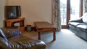 A living room with a leather sofa, a wooden coffee table, a television on a wooden stand, and a framed picture on the wall. - Baileys Barn - UKC3738 (Foxley, near Fakenham)