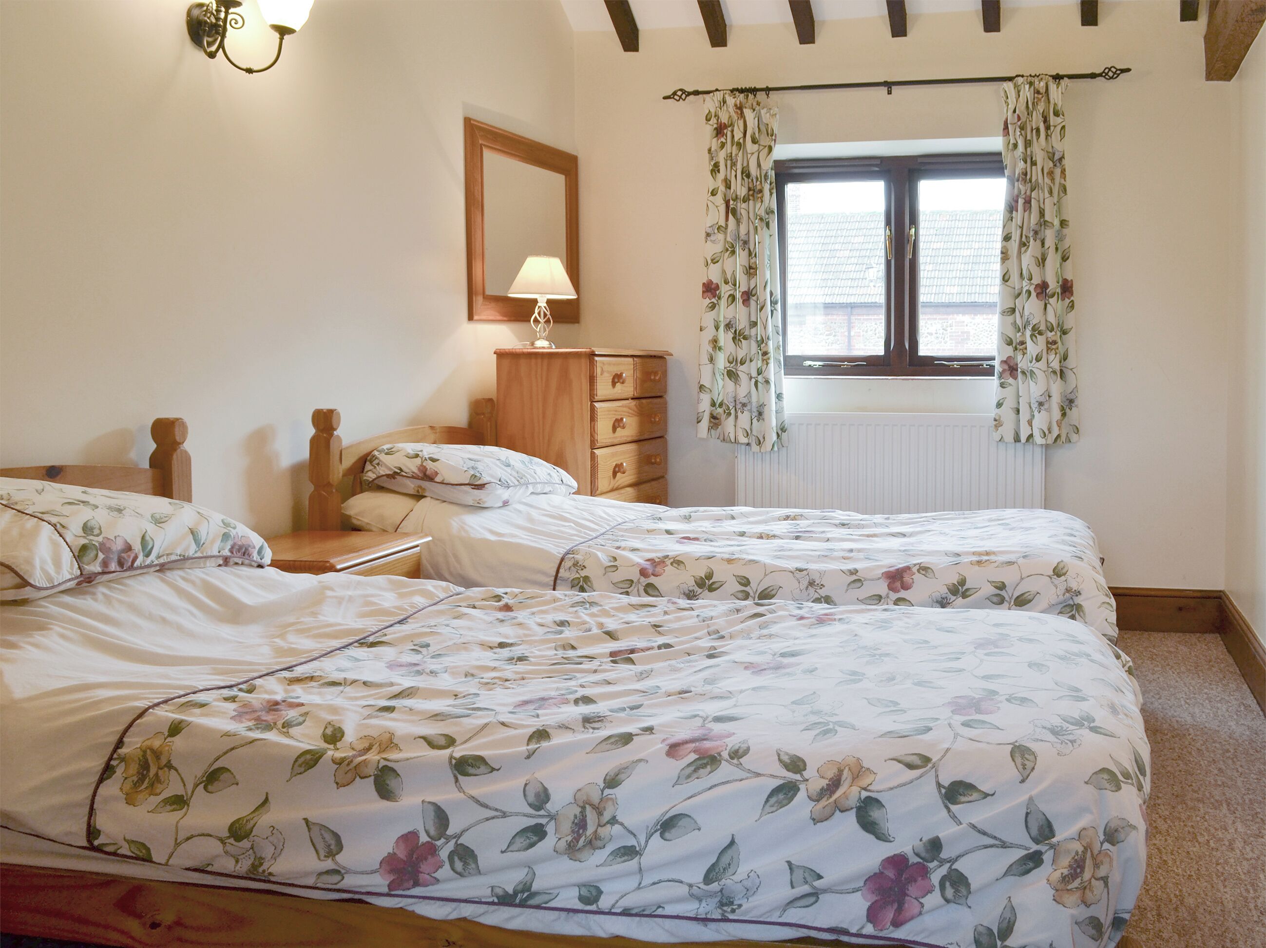 A bedroom with two beds, a dresser, a lamp, and a window with floral curtains.