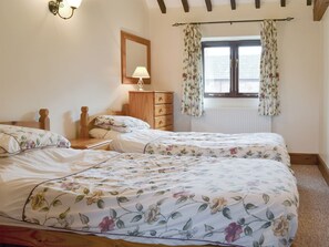 Une chambre avec deux lits, une commode, une lampe et une fenêtre ornée de rideaux à motifs floraux.