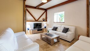 Ein geräumiges Wohnzimmer mit einem weißen Sofa, einem Holztisch und einem Fernseher auf einem Holzständer.