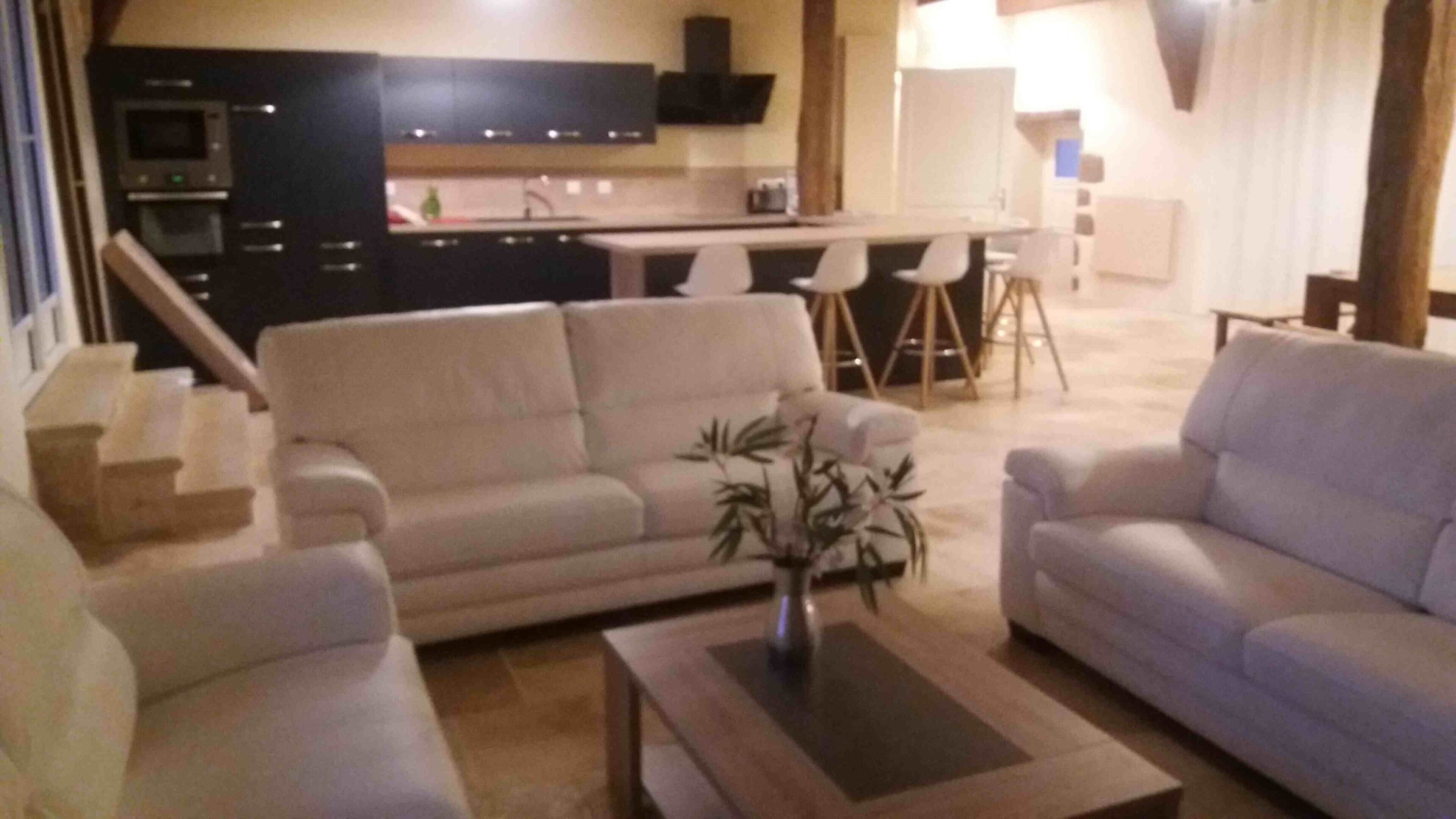 A living room with a sofa, armchairs, and a coffee table. There is a kitchen area with a microwave and cabinets in the background.