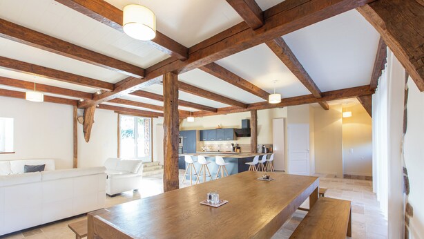Ein geräumiges Zimmer mit einem großen Holztisch, weißen Sofas und einer Küchenzeile im Hintergrund.