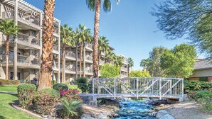 Un hôtel doté de nombreux balcons, d’un pont enjambant un ruisseau et de palmiers.