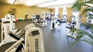 Une salle de sport équipée de divers appareils d’exercice, notamment des tapis de course et des appareils de musculation, disposés dans un espace vaste doté d’un sol recouvert de moquette et de grandes fenêtres.