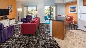 Une chambre d’hôtel moderne avec un canapé rouge, un fauteuil à rayures et un coin repas avec des chaises bleues.
