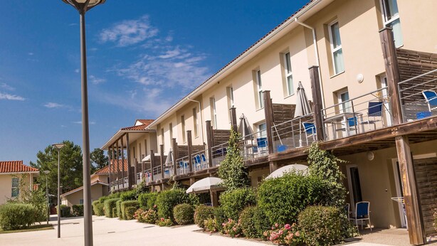 A row of hotel buildings with balconies, outdoor seating, and a clear blue sky. - Studio cosy et charmant 2p (Hourtin)
