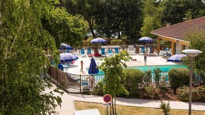 A pool area with lounge chairs and umbrellas, a sign indicating a no parking zone, and a building with a tiled roof. - Studio cosy et charmant 2p (Hourtin)