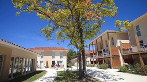 A courtyard with a tree, buildings with balconies, and a clear blue sky. - Studio cosy et charmant 2p (Hourtin)