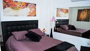 A bedroom with a large bed, a nightstand, a mirror, and two paintings on the wall. - BEAUTIFUL APARTMENT NEAR THE BEACH AND THE MOUNTAIN (Benalmádena)
