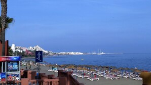 A beach with umbrellas and lounge chairs, a clear blue sky, and a distant cityscape. - BEAUTIFUL APARTMENT NEAR THE BEACH AND THE MOUNTAIN (Benalmádena)