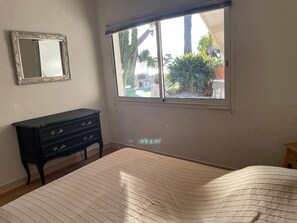 A bedroom with a bed, a dresser, a mirror, and a window with a view of a garden. - Panoramic Sea View - Pool - Quiet (Cagnes-sur-Mer)