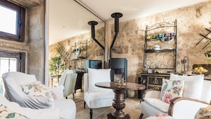 Un salon chaleureux avec des meubles recouverts de tissu blanc, une table ronde en bois et un mur en pierre.