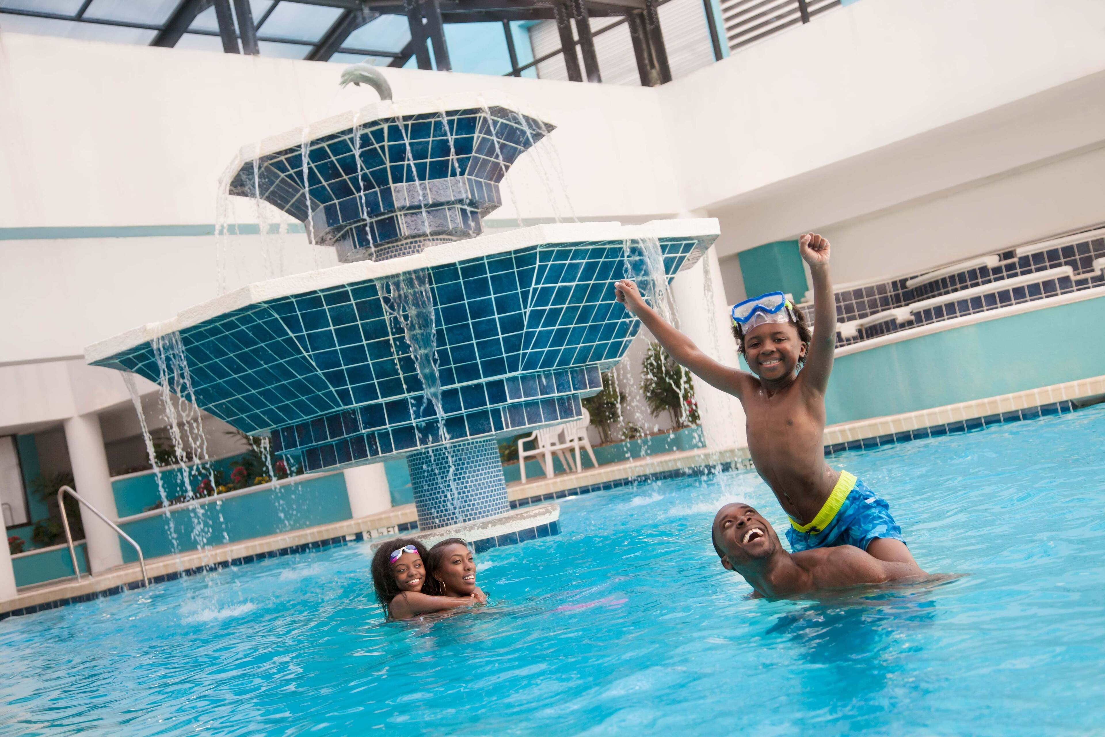An indoor swimming pool with a water fountain feature, a poolside seating area, and a modern architectural design.