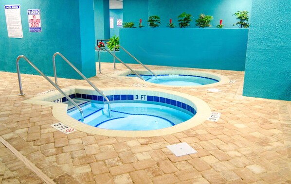 Dos piscinas interiores con bordes de azulejos azules, rodeadas de suelo de ladrillo y pared azul.