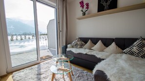 A living room with a sofa, a glass coffee table, a fluffy rug, a potted plant, and a view of a snowy landscape through a sliding glass door. - Finest Kitzblick Golf Suites TOP 2 (Zell am See)