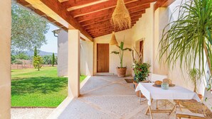 Un espace extérieur abrité, avec une table dressée pour les repas, entouré de plantes en pot et offrant une vue sur un paysage verdoyant.