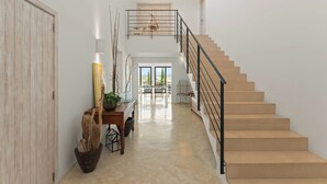 Un hall d’entrée spacieux avec un escalier en bois, un bureau agrémenté d’une plante et une vue sur l’extérieur.