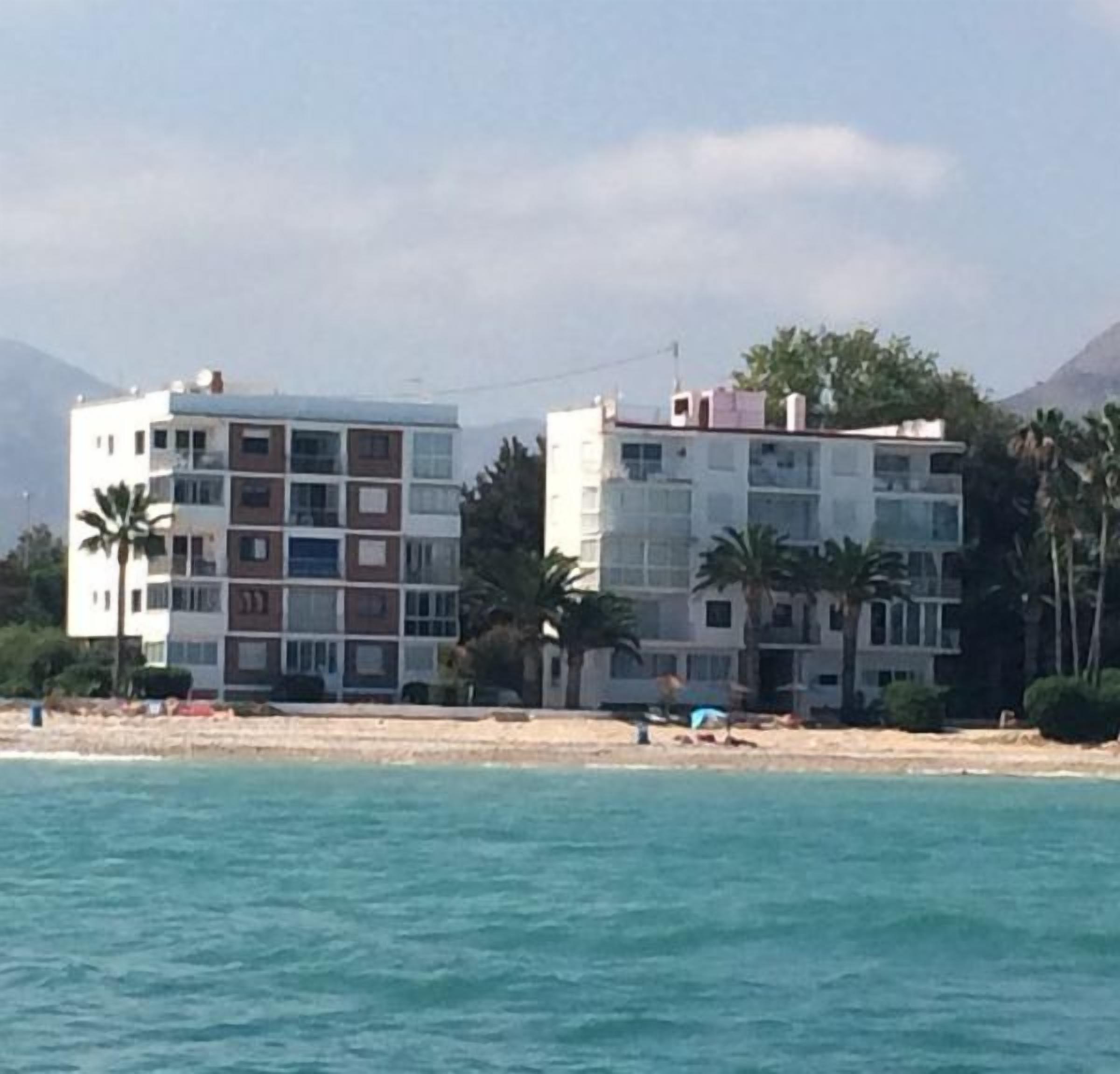 Un edificio costero de varios pisos, con balcones y una playa al fondo.
