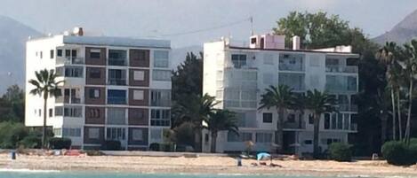 Un edificio costero de varios pisos, con balcones y una playa al fondo.