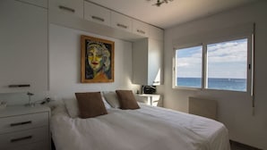 Ein Schlafzimmer mit einem Bett, einem Nachttisch, einem Schreibtisch, einem Stuhl, einem Bild und einem Fenster mit Meerblick.