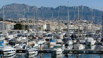 Una marina con numerosos barcos amarrados, rodeada de edificios y montañas al fondo.