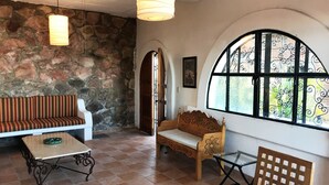 A cozy room with a stone wall, a wooden bench, a cushioned sofa, a small table, and a large window with decorative iron bars. - Spacious bright tiled 2 bedroom with Ocean View (Cerro)