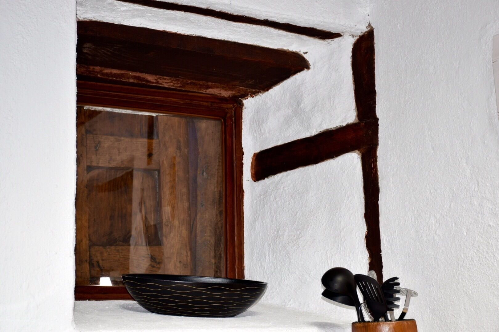 Une cuisine rustique avec une fenêtre en bois, un saladier noir et un porte-ustensiles.