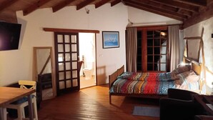 A cozy room with a wooden ceiling, a bed with a colorful blanket, a desk, and a chair. - We look forward to you! (La Vega)