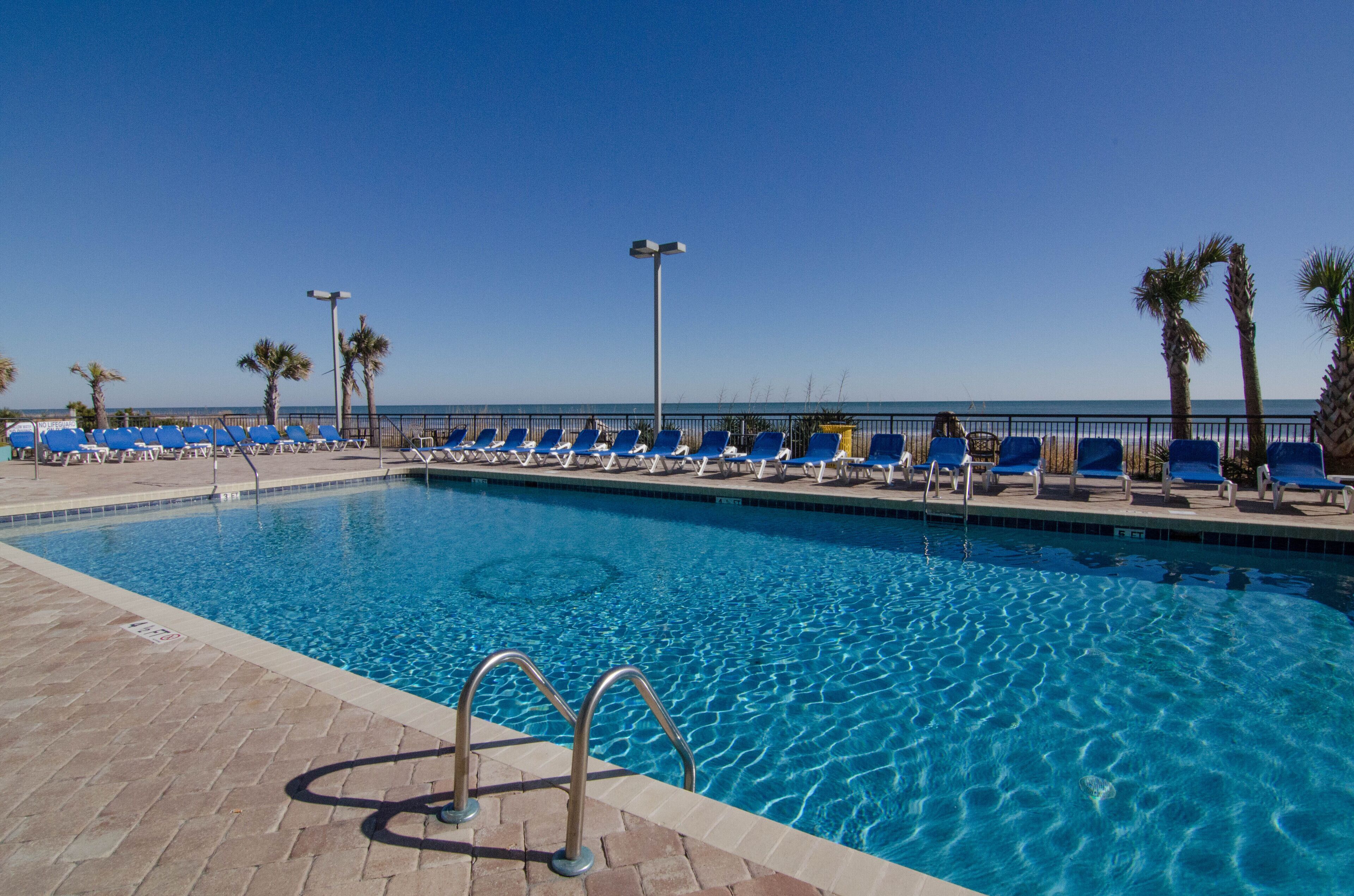 A swimming pool with blue lounge chairs and palm trees.