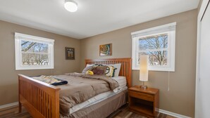 A bedroom with a wooden bed, two windows, a nightstand, and a wall-mounted lamp.