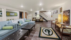 A living room with a couch, coffee table, and a rug with a logo, a staircase, and framed pictures on the walls.