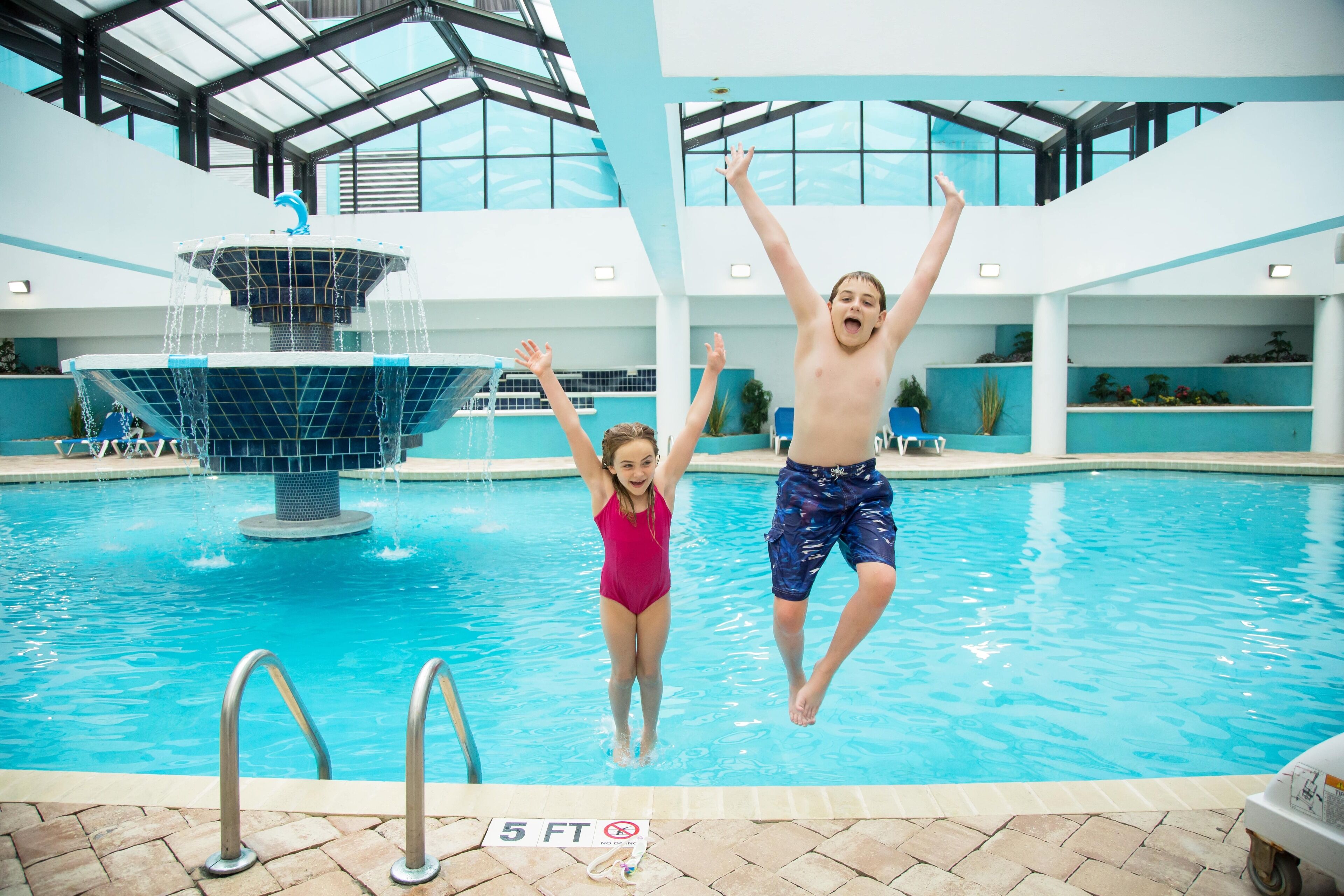 An indoor swimming pool with a diving platform and a fountain.