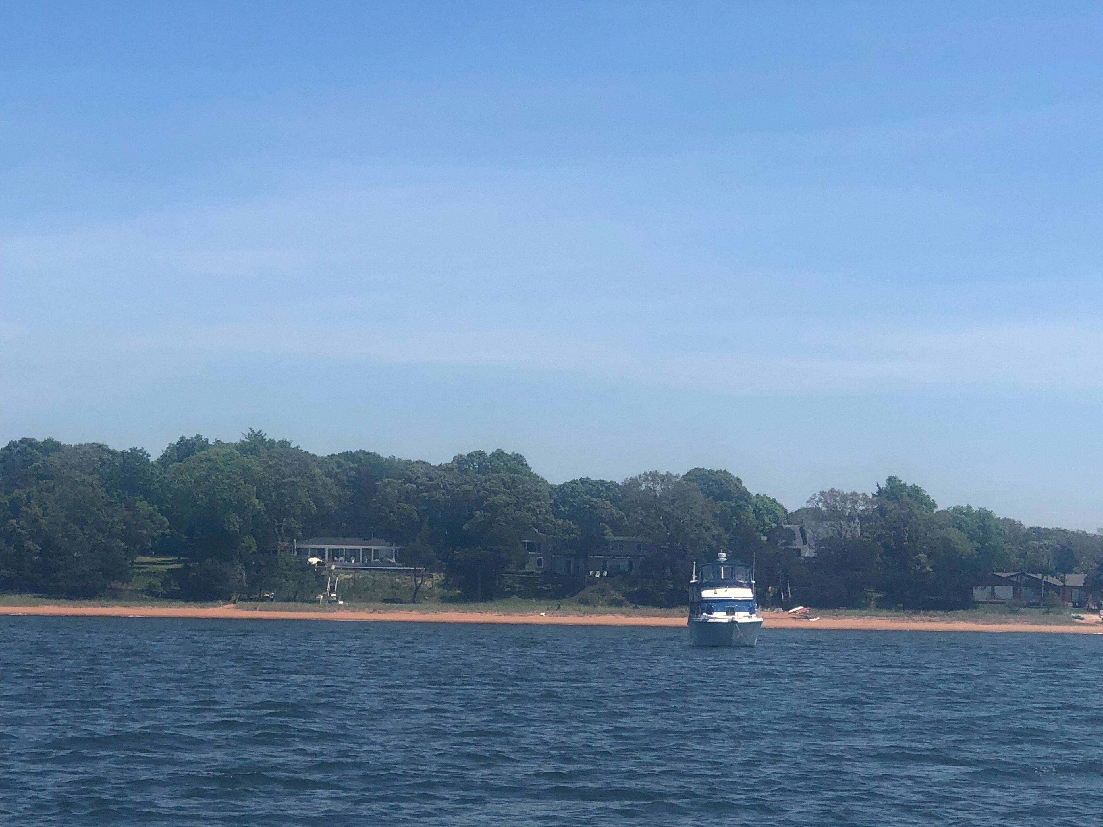 A boat on a calm body of water with a beach and houses in the background.