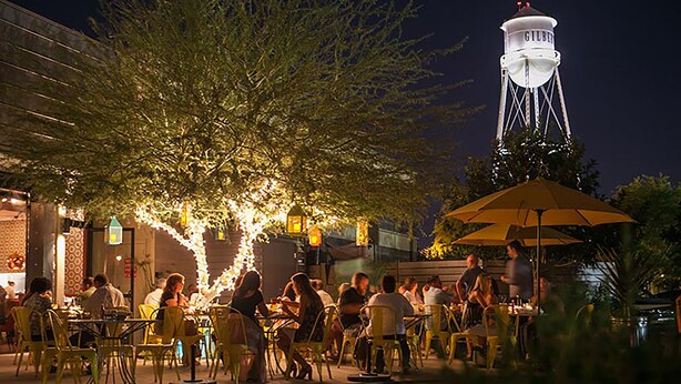 An outdoor dining area with yellow chairs and tables, a large umbrella, and a water tower in the background.