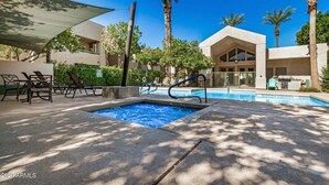 A pool area with lounge chairs, a hot tub, and palm trees.