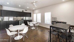 A spacious kitchen with dark cabinets, a white dining table with chairs, and a ceiling fan.