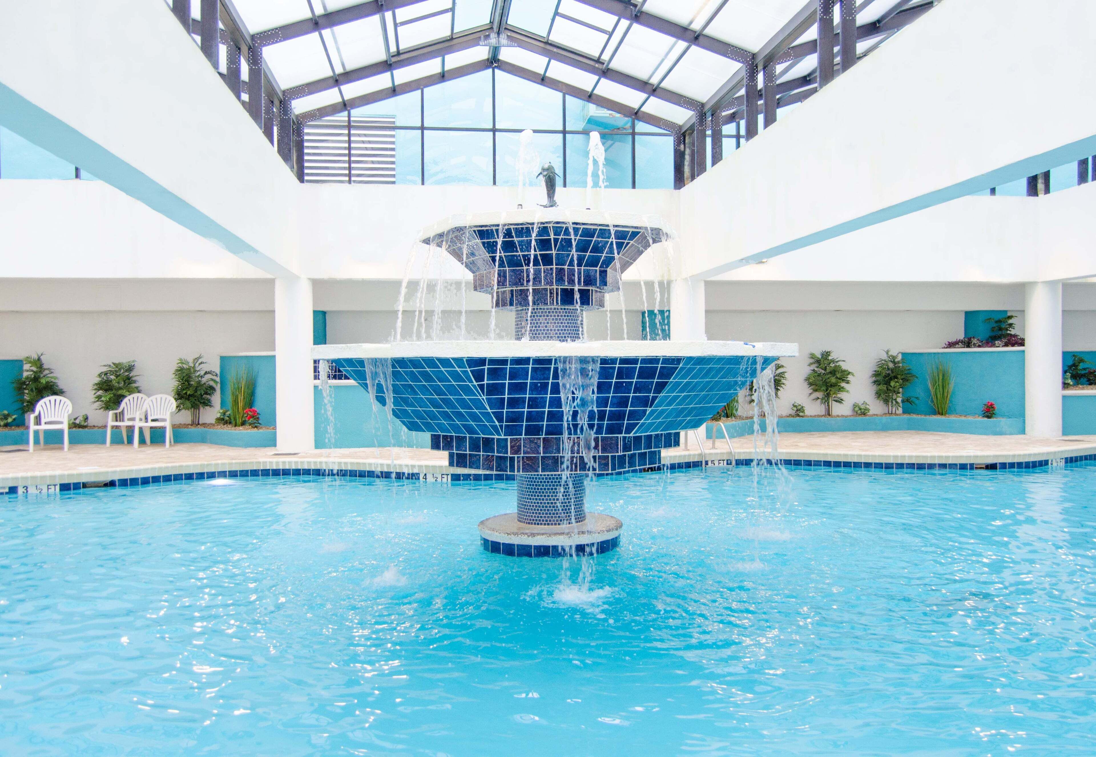 A large indoor pool with a central fountain, surrounded by white walls and blue-tiled edges.