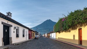 A cobblestone street lined with buildings, a mountain in the background, and a car parked on the side.
