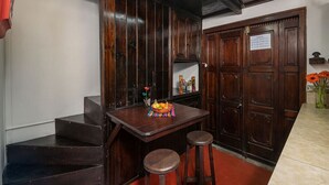 A kitchen with dark wooden cabinets, a wooden table with stools, and a small shelf with decorative items.
